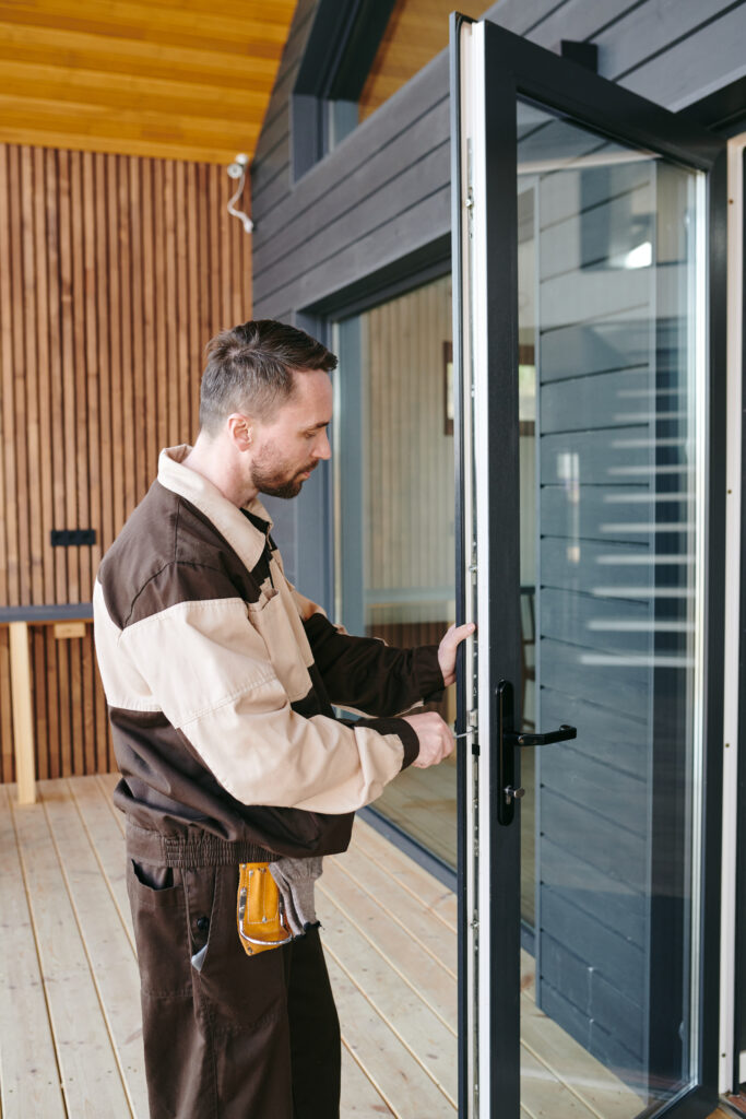 Young repairman standing in front of a glass door while repairing lock